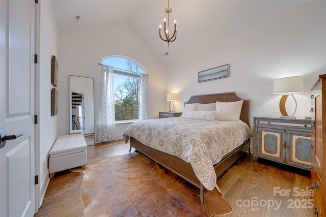 bedroom with a notable chandelier, high vaulted ceiling, and wood finished floors