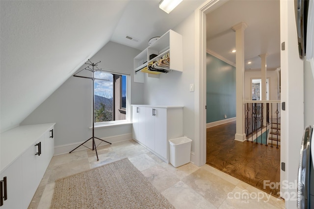 interior space featuring baseboards, lofted ceiling, visible vents, and decorative columns
