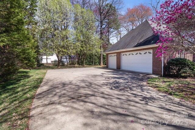 view of side of home with brick siding, a garage, driveway, and roof with shingles