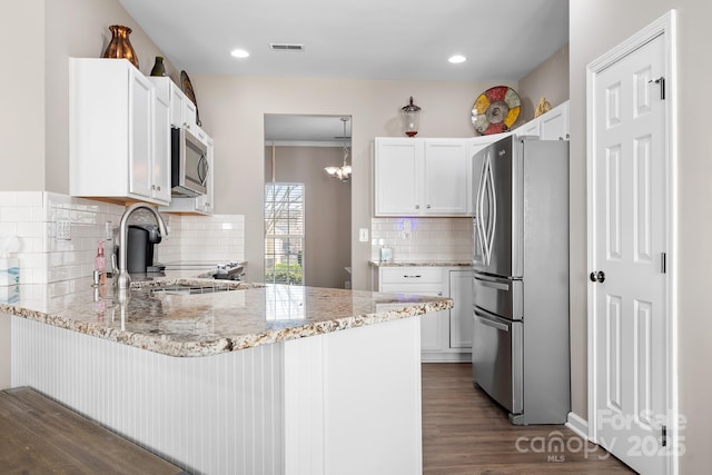 kitchen with light stone counters, visible vents, a peninsula, and stainless steel appliances