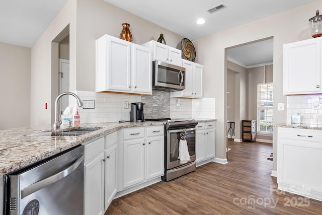kitchen featuring visible vents, a sink, light stone counters, wood finished floors, and appliances with stainless steel finishes