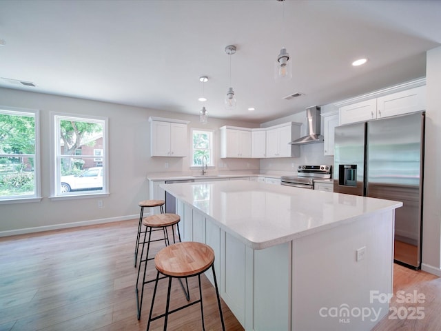 kitchen featuring appliances with stainless steel finishes, wall chimney exhaust hood, a kitchen island, white cabinets, and light wood-style floors