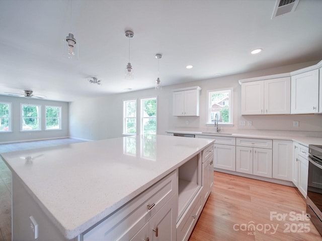 kitchen with a sink, healthy amount of natural light, white cabinets, light wood-style flooring, and recessed lighting