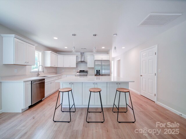 kitchen featuring stainless steel appliances, wall chimney exhaust hood, a sink, light wood finished floors, and recessed lighting