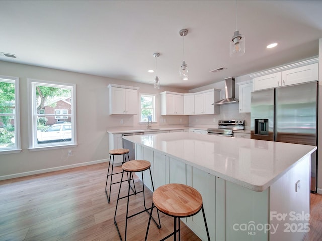 kitchen with wall chimney exhaust hood, appliances with stainless steel finishes, a center island, light wood-style flooring, and recessed lighting