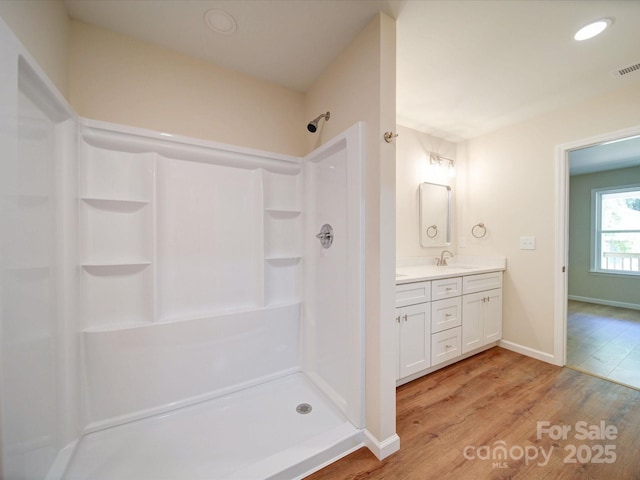 full bathroom with wood finished floors, a shower, vanity, and baseboards