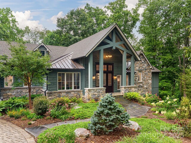 view of front of home with roof with shingles, a standing seam roof, covered porch, stone siding, and metal roof