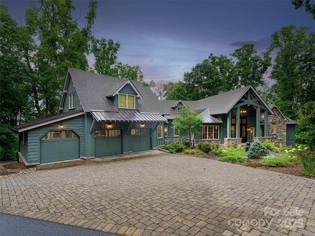 view of front of property featuring decorative driveway, stone siding, an attached garage, and a shingled roof
