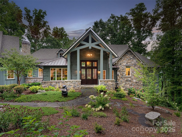 view of front of house with stone siding, a chimney, and a standing seam roof