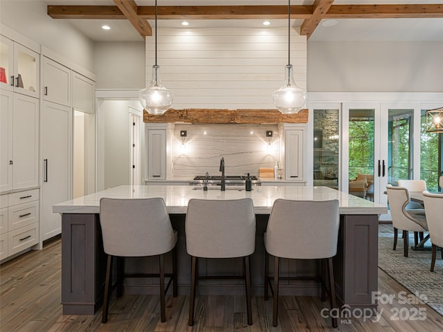 kitchen with tasteful backsplash, dark wood finished floors, an island with sink, beam ceiling, and white cabinetry