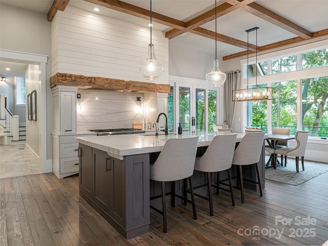 kitchen featuring a center island with sink, dark wood-type flooring, a kitchen breakfast bar, beamed ceiling, and backsplash