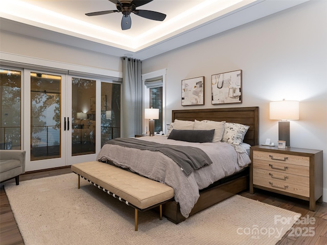 bedroom featuring a tray ceiling, wood finished floors, a ceiling fan, and access to outside