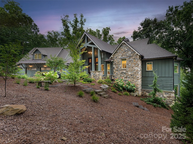 view of front facade featuring stone siding, board and batten siding, and roof with shingles