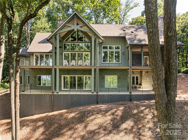 back of property with board and batten siding, roof with shingles, a chimney, a balcony, and a patio