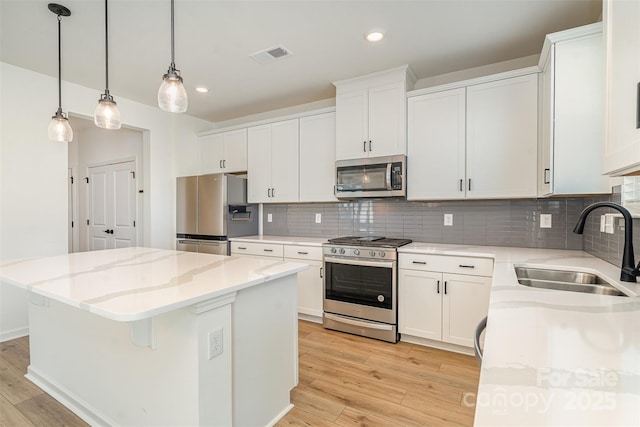 kitchen with light wood-style flooring, tasteful backsplash, a kitchen island, a sink, and stainless steel appliances