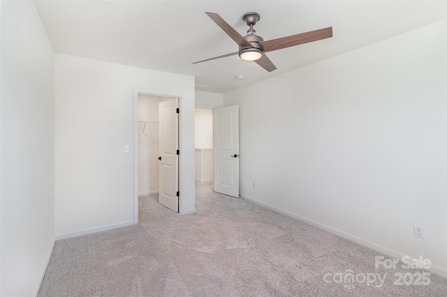 unfurnished bedroom featuring a walk in closet, carpet flooring, baseboards, and a ceiling fan