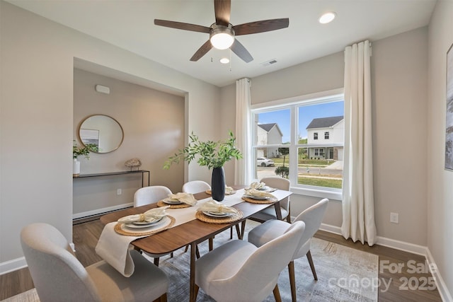 dining room with wood finished floors, visible vents, a ceiling fan, and baseboards