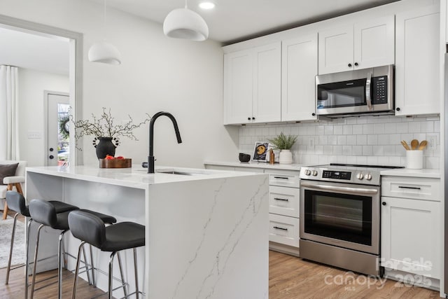 1749 Archdale Dr, Charlotte, NC 28210 - kitchen featuring appliances with stainless steel finishes, backsplash, a kitchen breakfast bar, white cabinetry, and hanging light fixtures