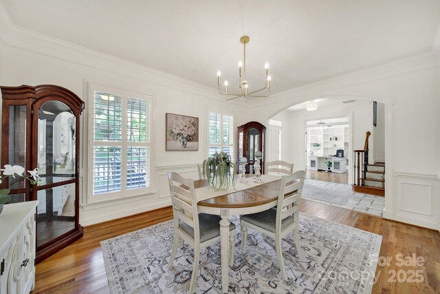 dining space with crown molding, arched walkways, and light wood-style flooring