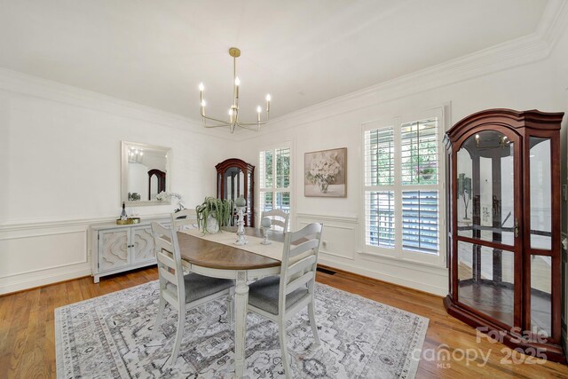 dining room with wood finished floors, ornamental molding, a wainscoted wall, and a chandelier
