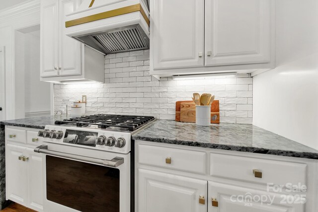 kitchen featuring custom range hood, dark stone counters, white cabinetry, and white gas stove