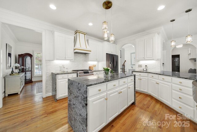 kitchen featuring arched walkways, a center island, stainless steel appliances, custom range hood, and tasteful backsplash