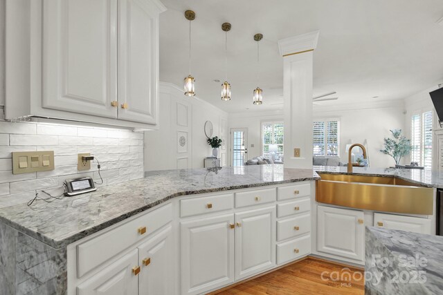 kitchen with white cabinets, light stone countertops, a sink, open floor plan, and backsplash