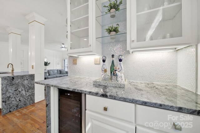bar with ceiling fan, decorative columns, decorative backsplash, wood finished floors, and wine cooler