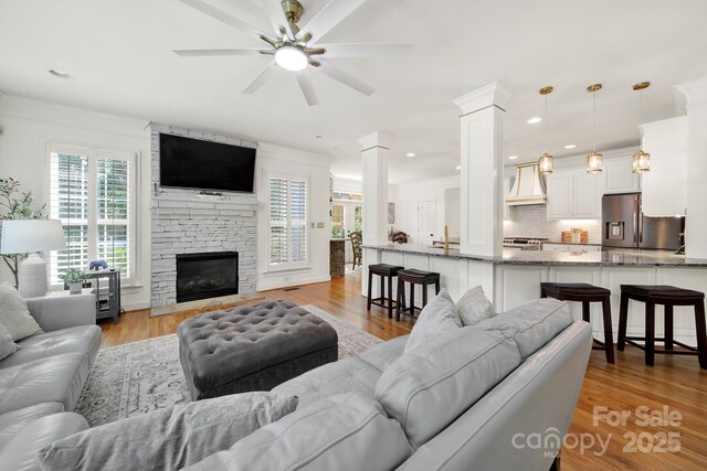 living area with ornate columns, a ceiling fan, light wood finished floors, and a fireplace
