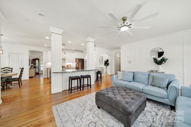 living area with crown molding, ceiling fan, ornate columns, and light wood-style flooring