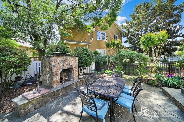 view of patio / terrace with an outdoor stone fireplace, fence, and outdoor dining space