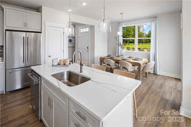 kitchen with a sink, light stone countertops, dark wood-style flooring, stainless steel appliances, and a kitchen island with sink