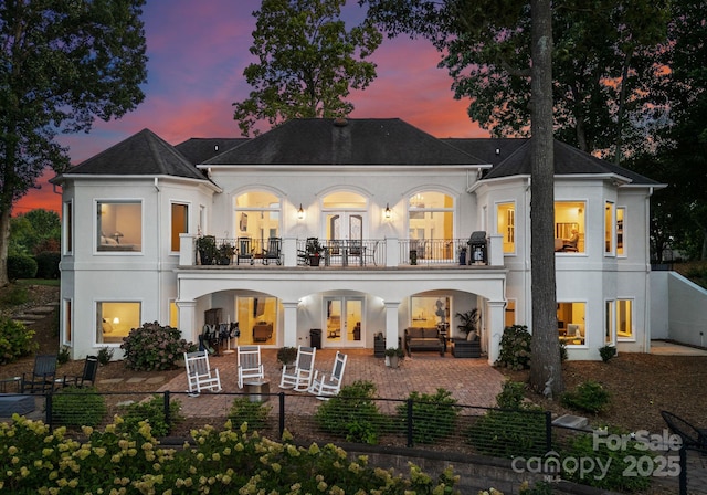 102 Stone Point Ct, Mooresville, NC 28117 - back of property at dusk with french doors, a fenced front yard, stucco siding, and a balcony