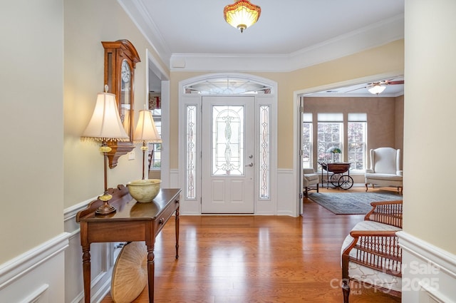 entrance foyer with a wainscoted wall, crown molding, wood finished floors, ceiling fan, and a decorative wall