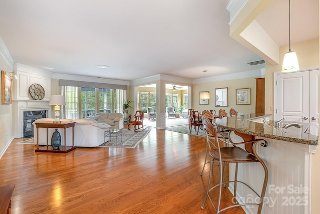 living area with a ceiling fan, light wood finished floors, a fireplace, ornamental molding, and visible vents