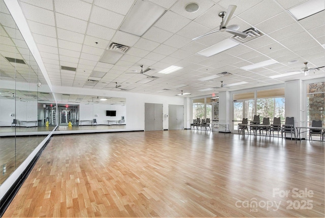interior space featuring a drop ceiling, a ceiling fan, wood finished floors, and visible vents