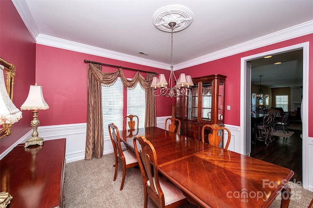 carpeted dining room with a wainscoted wall, a notable chandelier, visible vents, and ornamental molding