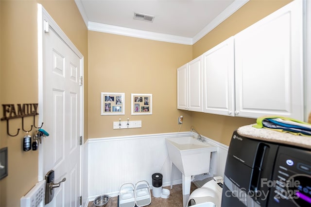 clothes washing area with visible vents, cabinet space, a wainscoted wall, and ornamental molding