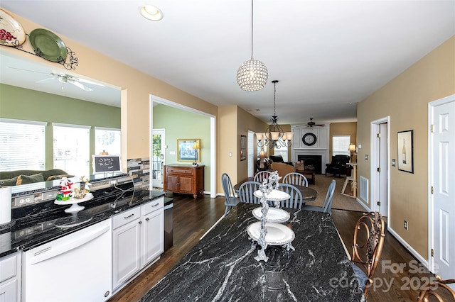 dining space with a wealth of natural light, ceiling fan with notable chandelier, a fireplace, and dark wood-type flooring