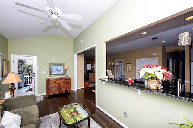 living room with wood finished floors, ceiling fan with notable chandelier, baseboards, and vaulted ceiling