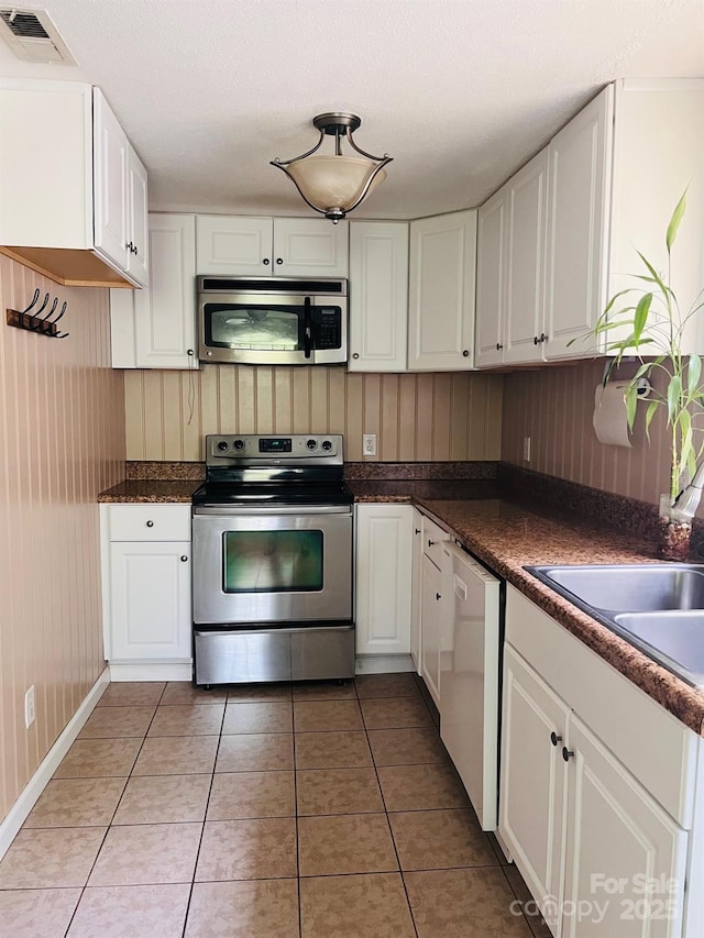 3232 Wilson Heights Dr, Hildebran, NC 28637 - kitchen with appliances with stainless steel finishes, white cabinets, dark countertops, light tile patterned flooring, and wooden walls