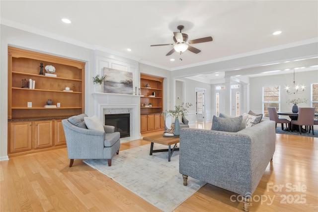 living area with recessed lighting, a high end fireplace, light wood-style flooring, and ceiling fan with notable chandelier
