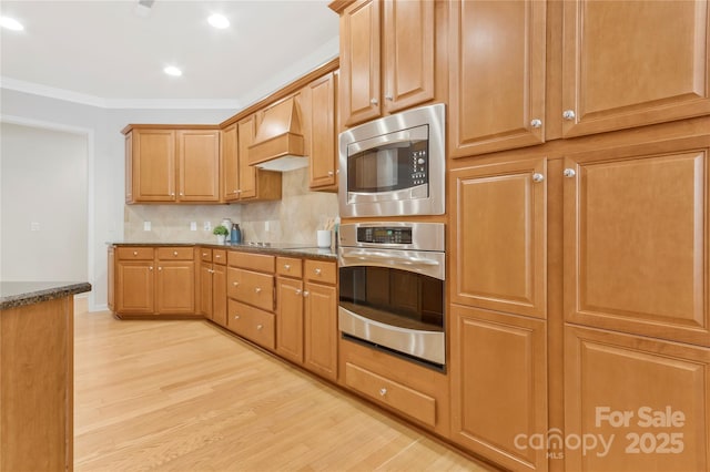 kitchen with light wood-style floors, crown molding, dark stone countertops, custom exhaust hood, and stainless steel appliances