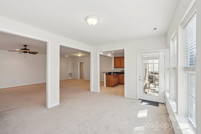 unfurnished living room featuring baseboards, light carpet, a ceiling fan, visible vents, and a sink