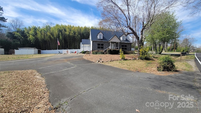 view of front of home with aphalt driveway, stone siding, and metal roof