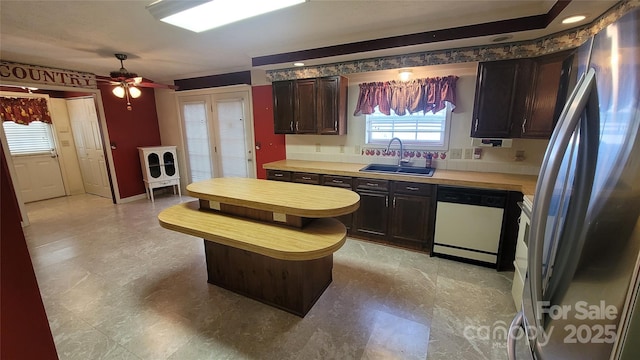 kitchen with a ceiling fan, freestanding refrigerator, a sink, light countertops, and dishwasher