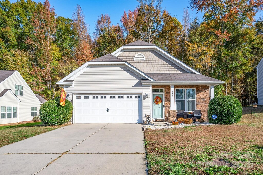 view of front of property with stone siding, roof with shingles, concrete driveway, a front yard, and a garage