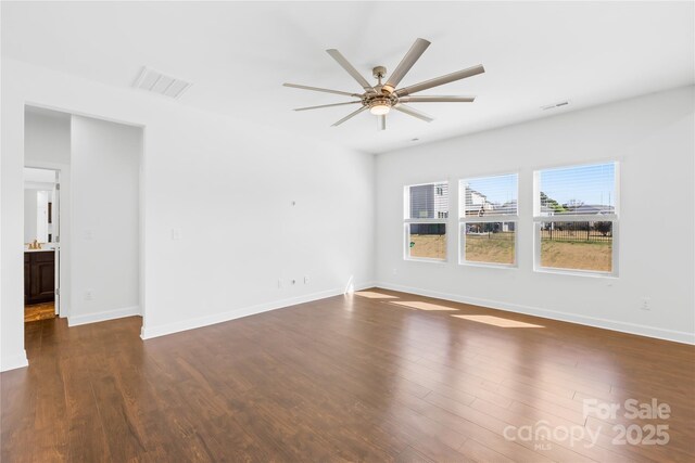 empty room with dark wood-type flooring, a ceiling fan, and visible vents