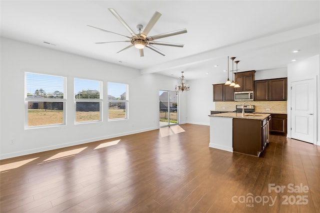 kitchen with stainless steel microwave, a sink, open floor plan, decorative backsplash, and dark wood-style flooring