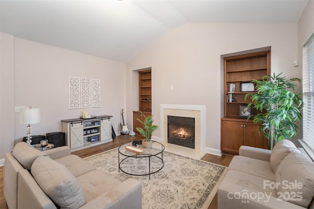 living area with built in shelves, baseboards, vaulted ceiling, a fireplace, and wood finished floors